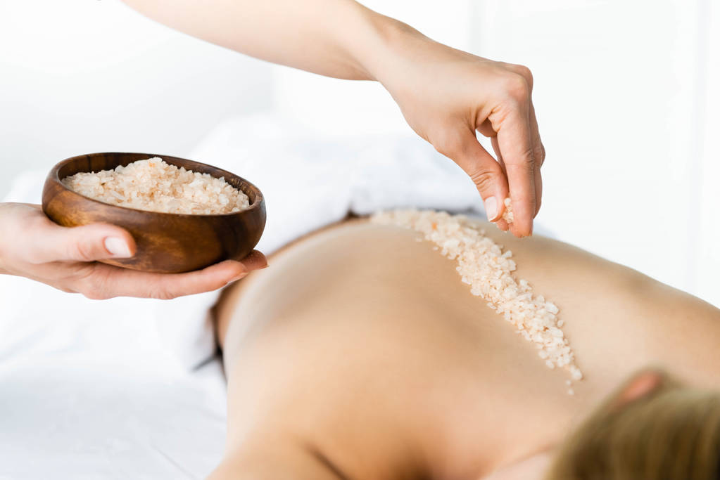 cropped view masseur applying sea salt back woman