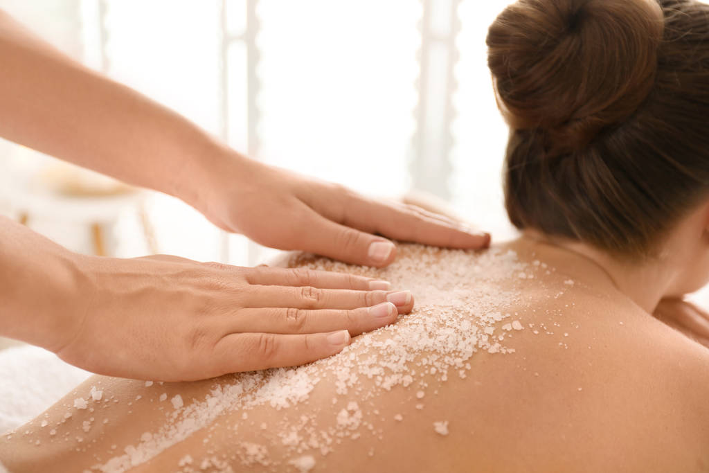 young woman having body scrubbing procedure with sea salt in spa